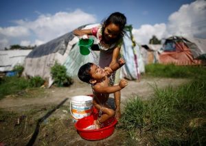 A girl showers her sister at the displacement camp for earthquake victims at Chuchepati in Kathmandu, Nepal, September 19, 2016. Picture taken September 19, 2016. To match Insight NEPAL-QUAKE/POLITICS Thomson Reuters Foundation/Navesh Chitrakar  - RTST7C9